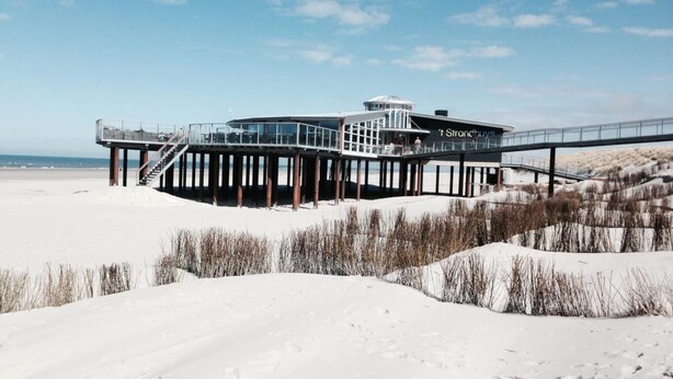 Et hotel ved stranden med en glasstruktur, en moler og udsigt over stranden.
