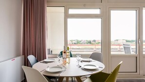 Et hotelværelse med et spisebord dækket til fire personer, en vinflaske og udsigt til en rød løber.