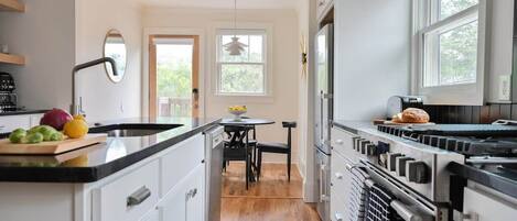 A modern kitchen with white cabinetry, a black countertop, and a built-in oven. There is a dining area with a table and chairs, and a window providing natural light.