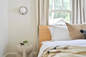 A neatly arranged bedroom with a bed, a bedside table with books, and a window with curtains. - Coming in Hot (Atlanta)