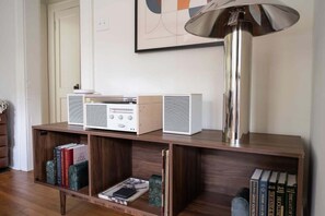 Ein modernes Wohnzimmer mit einem Holzkonsolentisch, einem weißen Radio, einer großen Stehlampe und Bücherregalen voller Bücher.