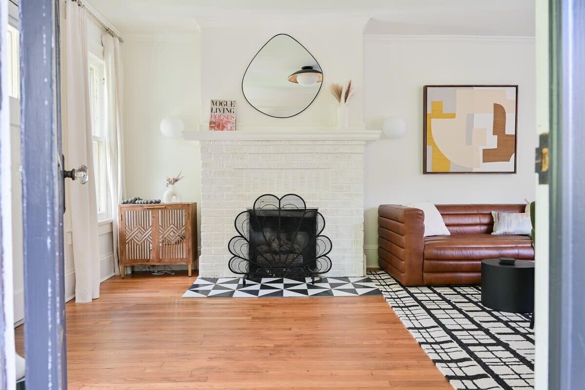 A living room with a white fireplace, a brown leather sofa, a black metal fireplace screen, and a patterned rug.