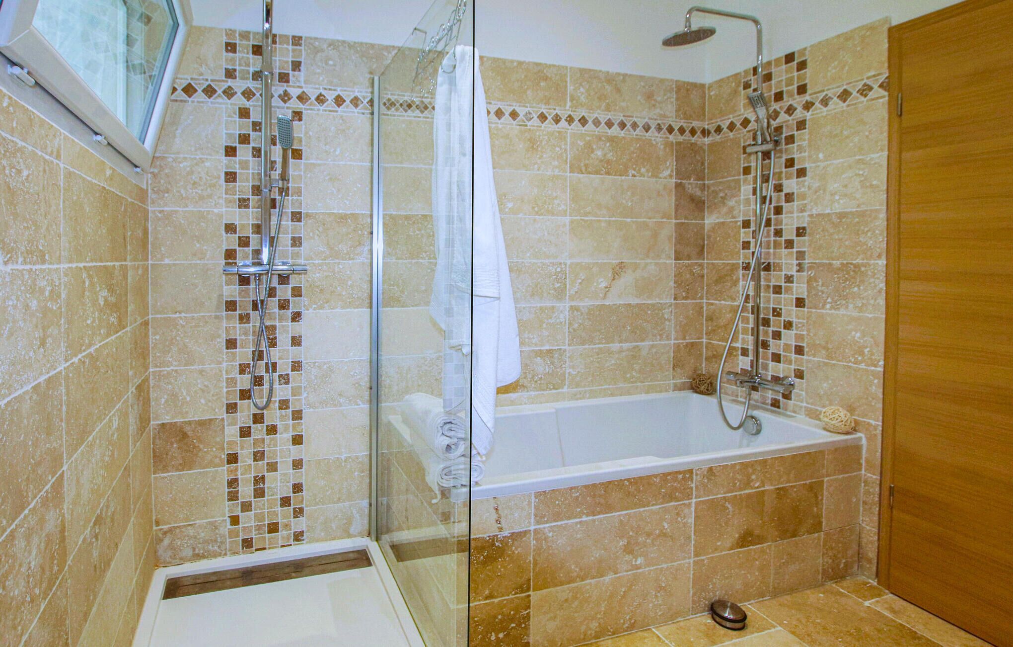 A bathroom with a glass shower enclosure, a bathtub, and tiled walls.