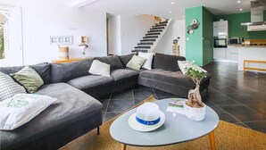 A modern living room with a grey sectional sofa, a round coffee table, and a staircase leading to a kitchen area. - Beautiful home in Suze-La-Rousse (Suze-La-Rousse)