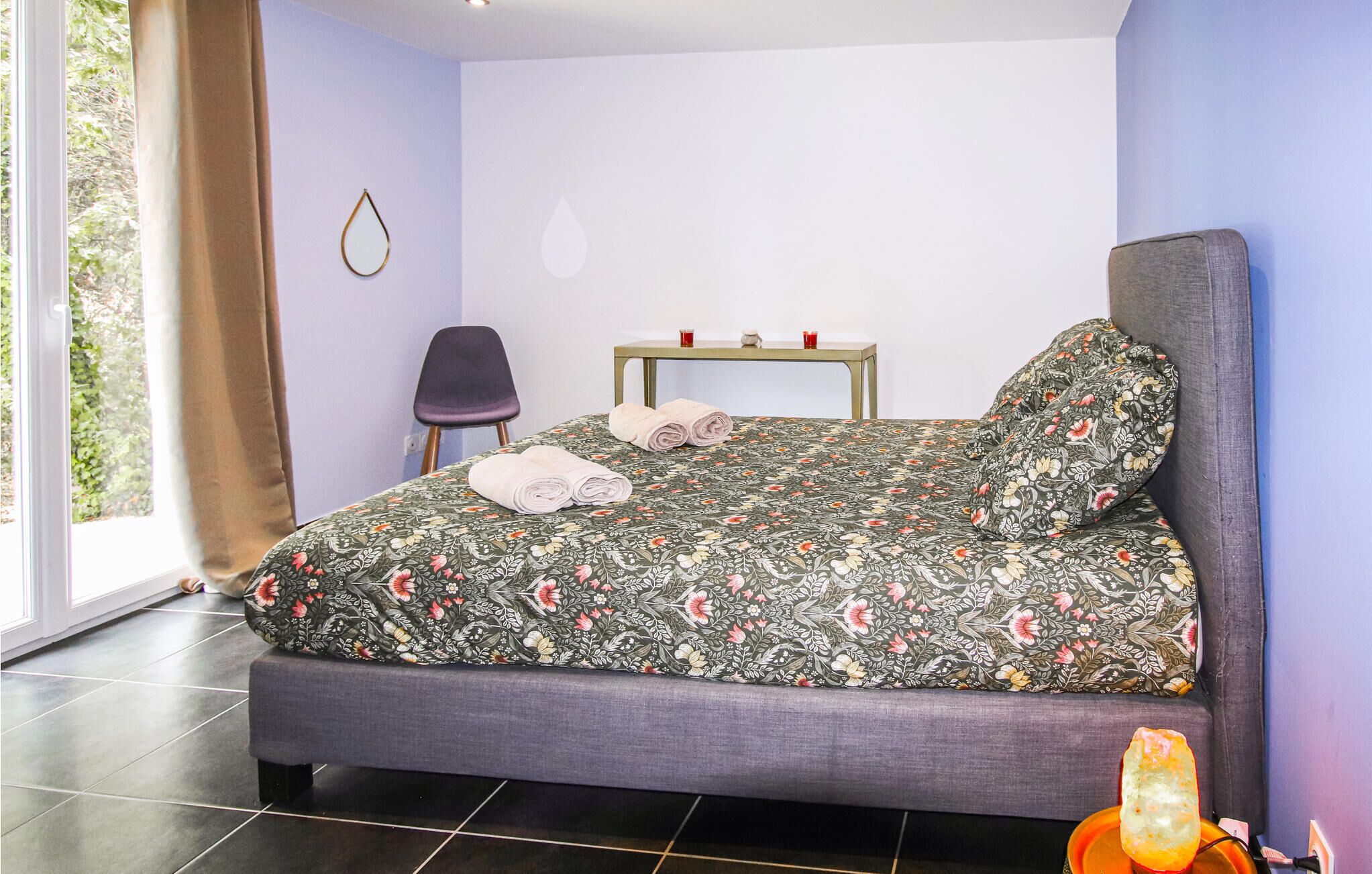 Ein Schlafzimmer mit einem Bett, einem Sessel, einem Tisch mit zwei roten Tassen und einem Fenster mit Vorhängen.
