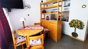 Een gezellige keuken met houten meubels, een eettafel, stoelen, een aan de muur bevestigde televisie en een klein plantje.