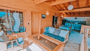Interior de una cabaña de madera con sofá, sillas, una mesa de comedor y una zona de cocina.
