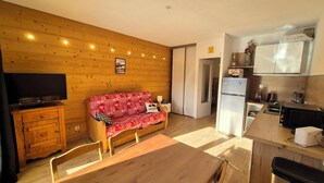 Ein gemütlicher Wohnbereich mit einer Holzwand, einem roten, gemusterten Sofa, einem Holzschrank und einem Fernseher.