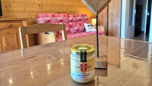 Ein Holztisch mit einem Glas Miel de Forêt, einer hölzernen herzförmigen Dekoration und einem rot-weißen Kissen auf einer Holzdauer in der Ferne.