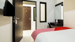 A hotel room with a bed, a desk, a TV, and a door. - OYO 3826 Columbus Residence K11 (Karawang)