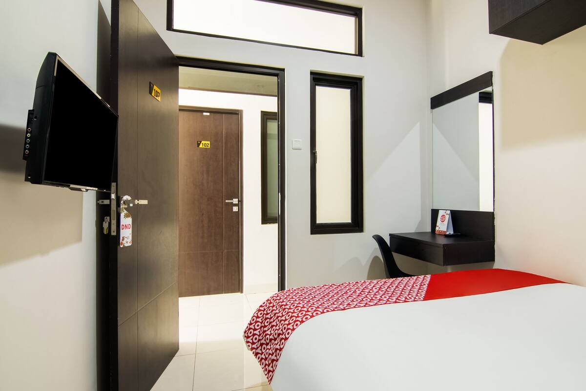 A hotel room with a bed, a desk, a TV, and a door.