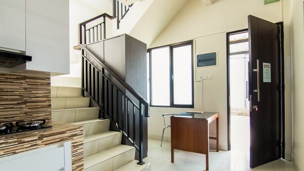 A modern kitchen with a wooden countertop, a built-in stove, and a staircase with a black railing. - OYO 3826 Columbus Residence K11 (Karawang)