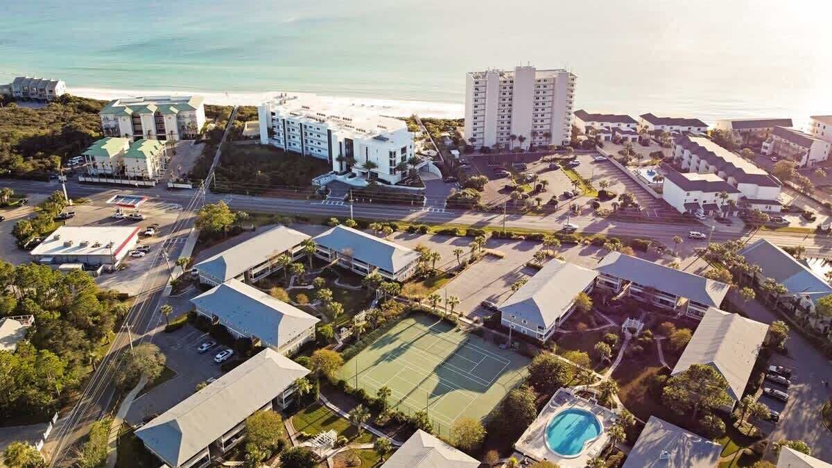 Luftaufnahme eines Küstenresorts mit mehreren Gebäuden, einem Tennisplatz und einem Schwimmbad.