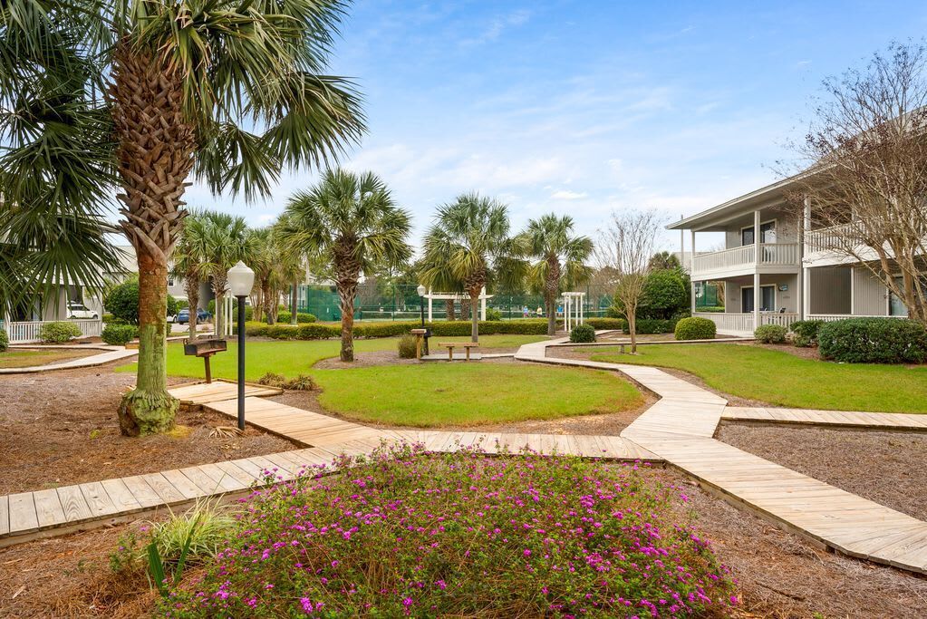 A landscaped courtyard with palm trees, a flower bed, and a wooden walkway leading to a building with a balcony.