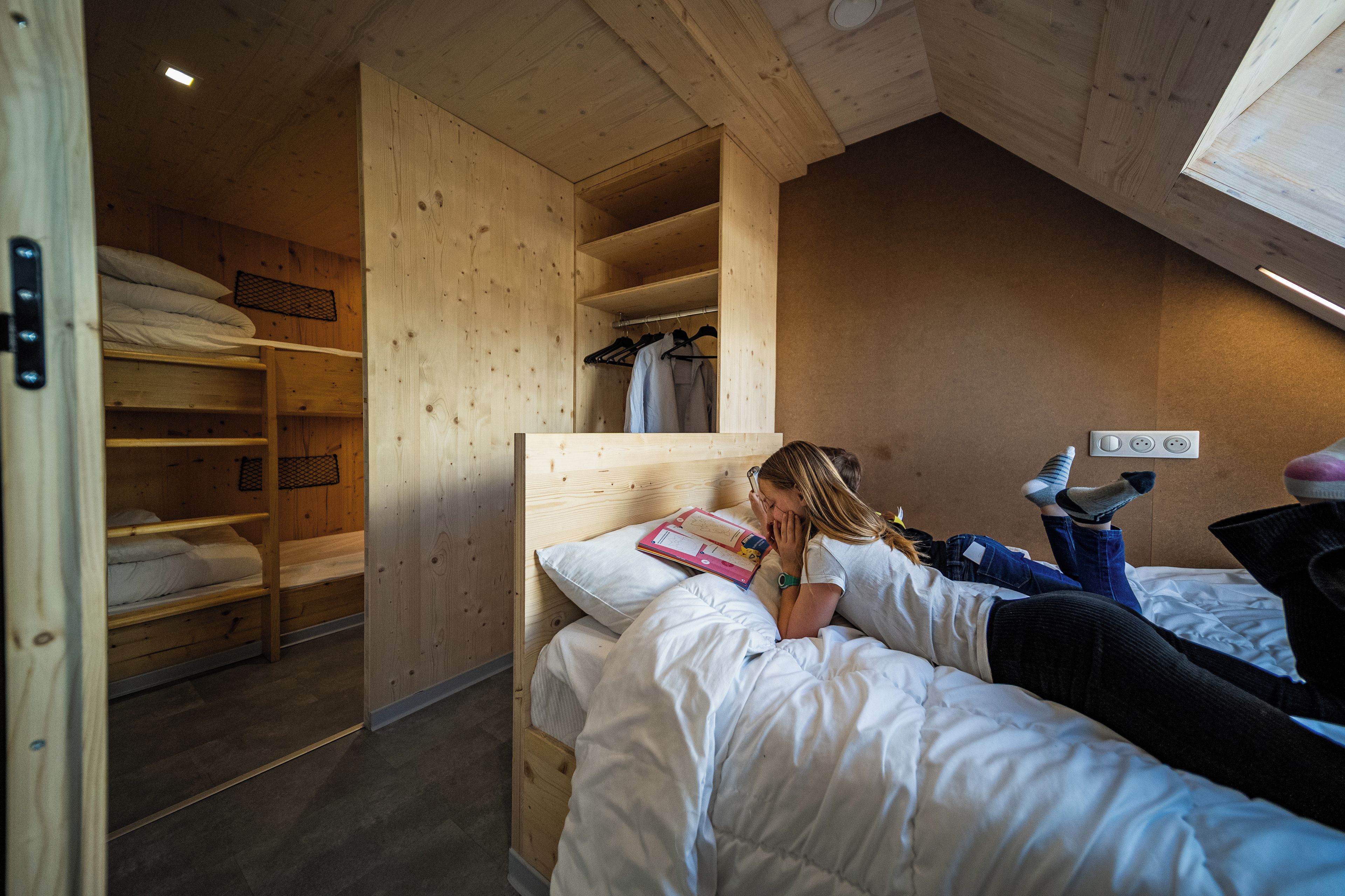 A room with bunk beds, a wooden wardrobe, and a ceiling with a skylight.