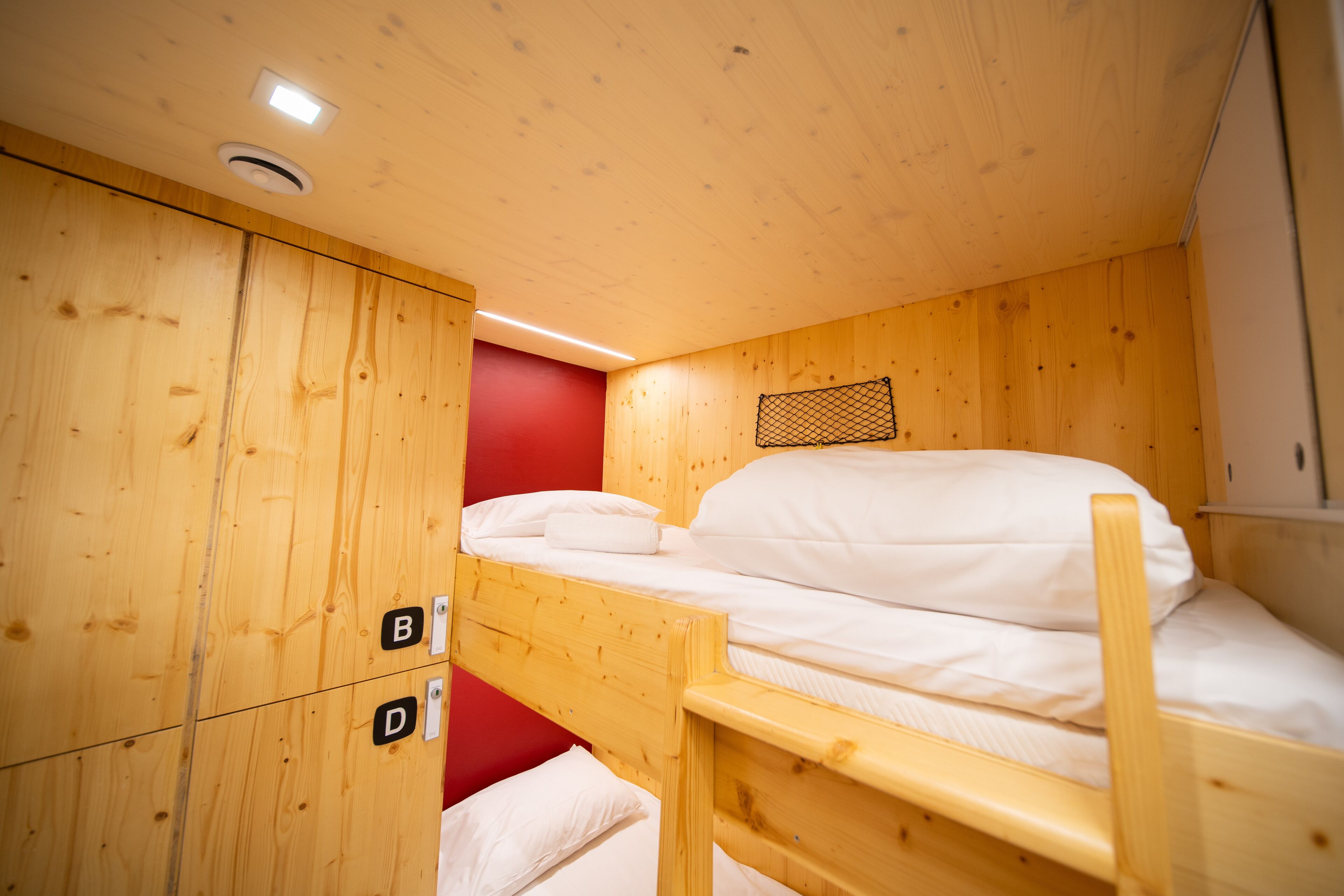 A bunk bed with a red wall and wooden paneling.