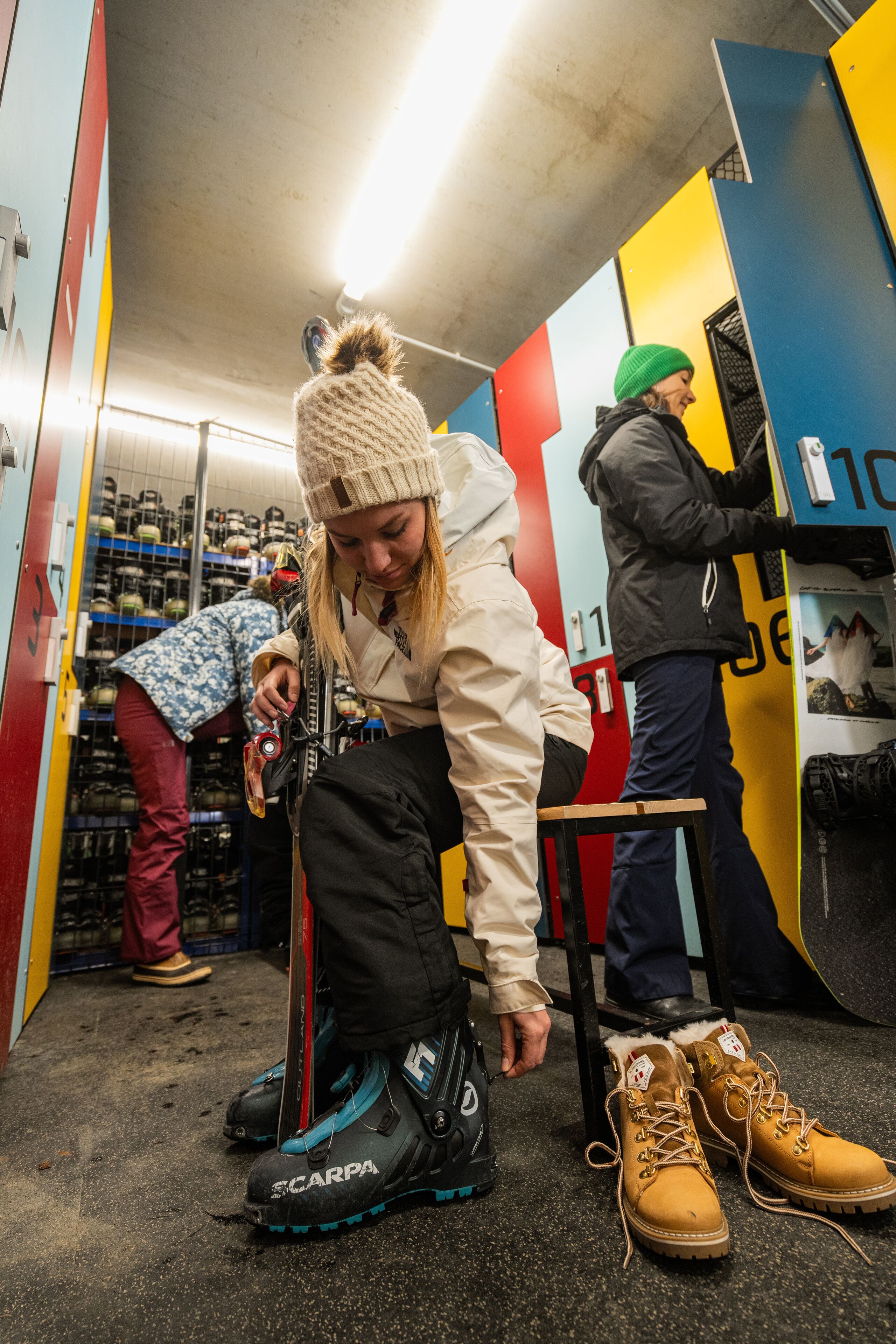 A person adjusting a snowboard in a brightly colored indoor setting with shelves of items in the background.