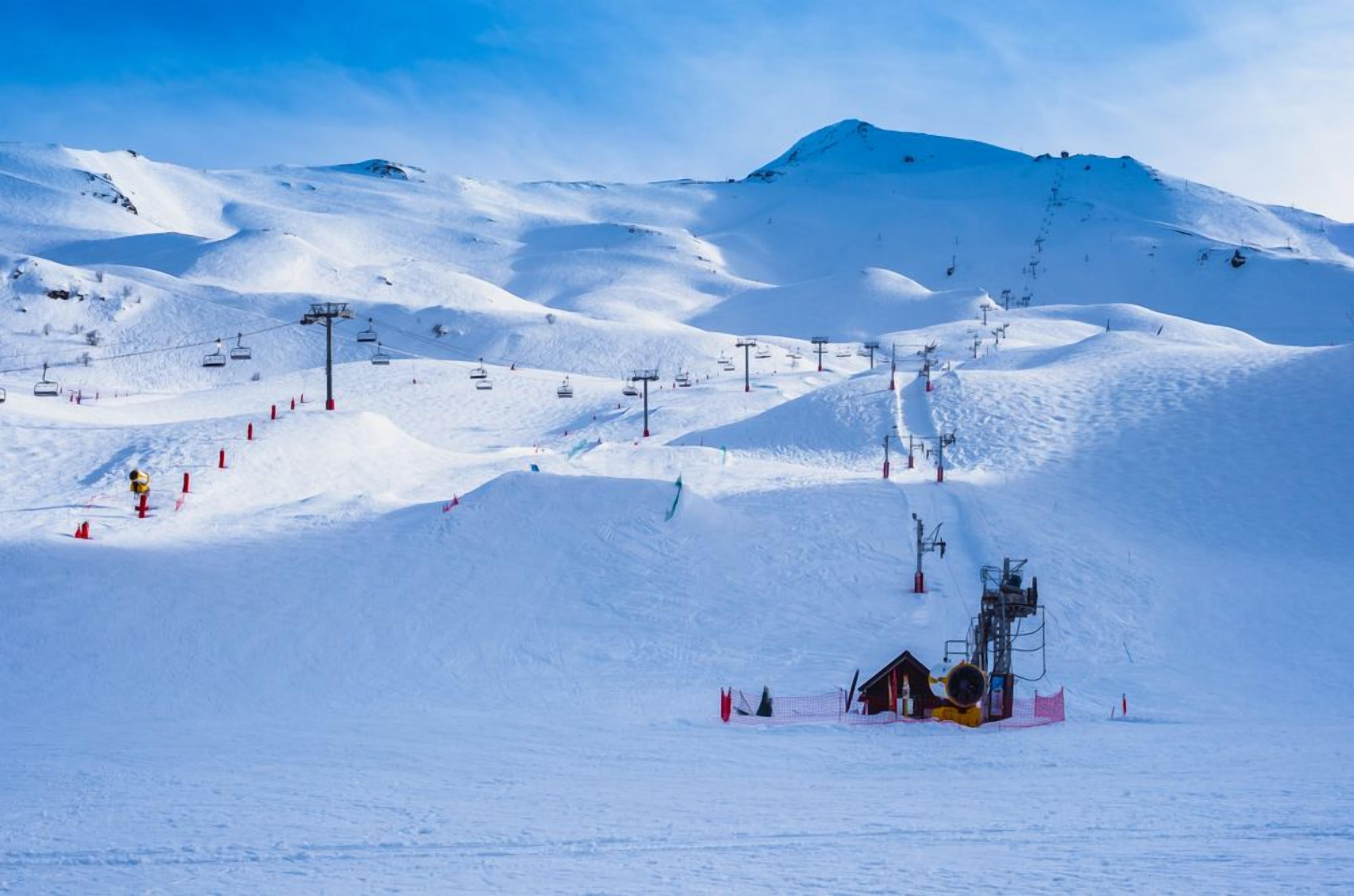 Une piste de ski enneigée, avec des remontées mécaniques et un petit chalet.