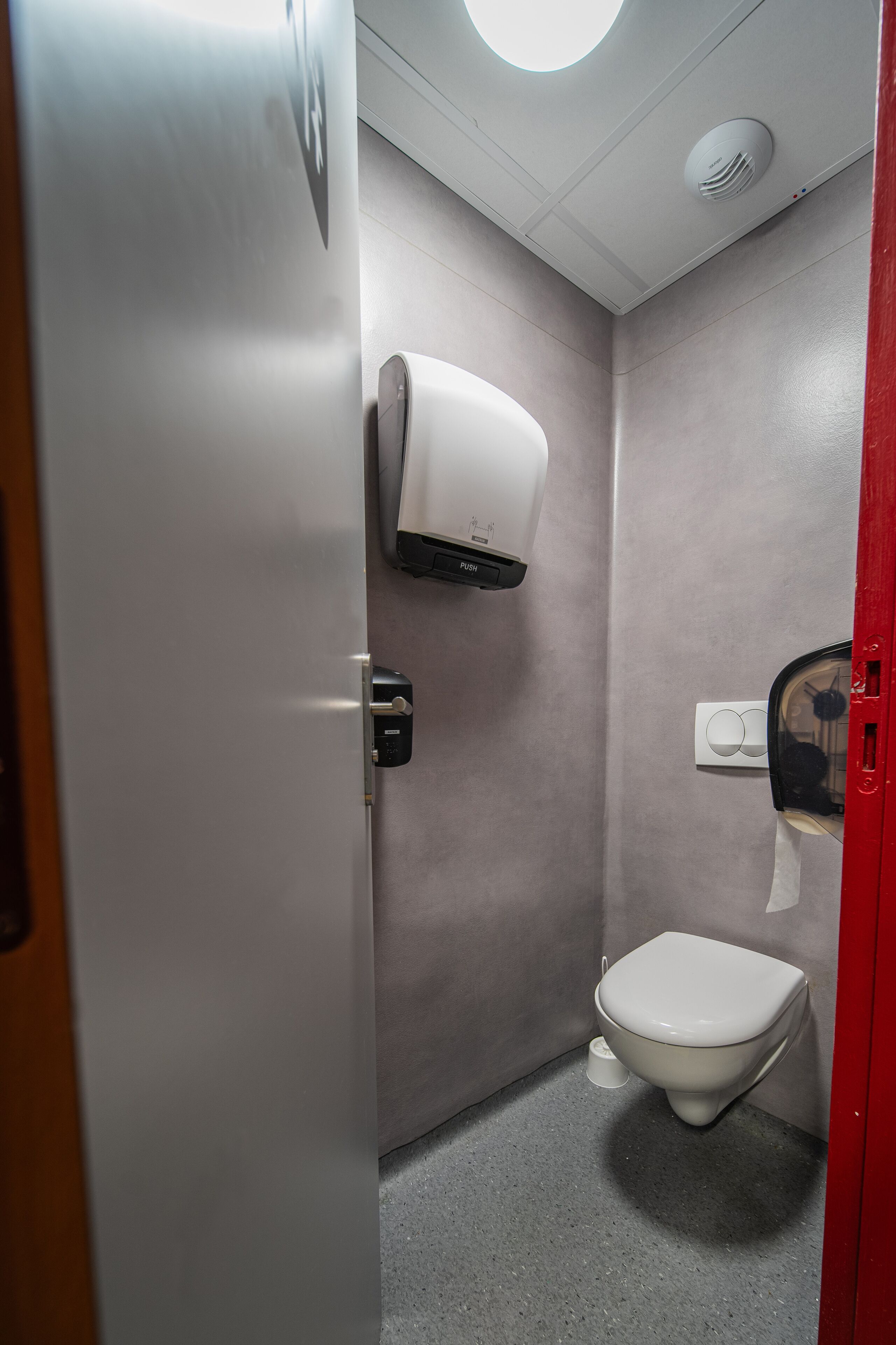 Un baño pequeño y moderno con un inodoro, un secador de manos y un dispensador de toallas de papel.