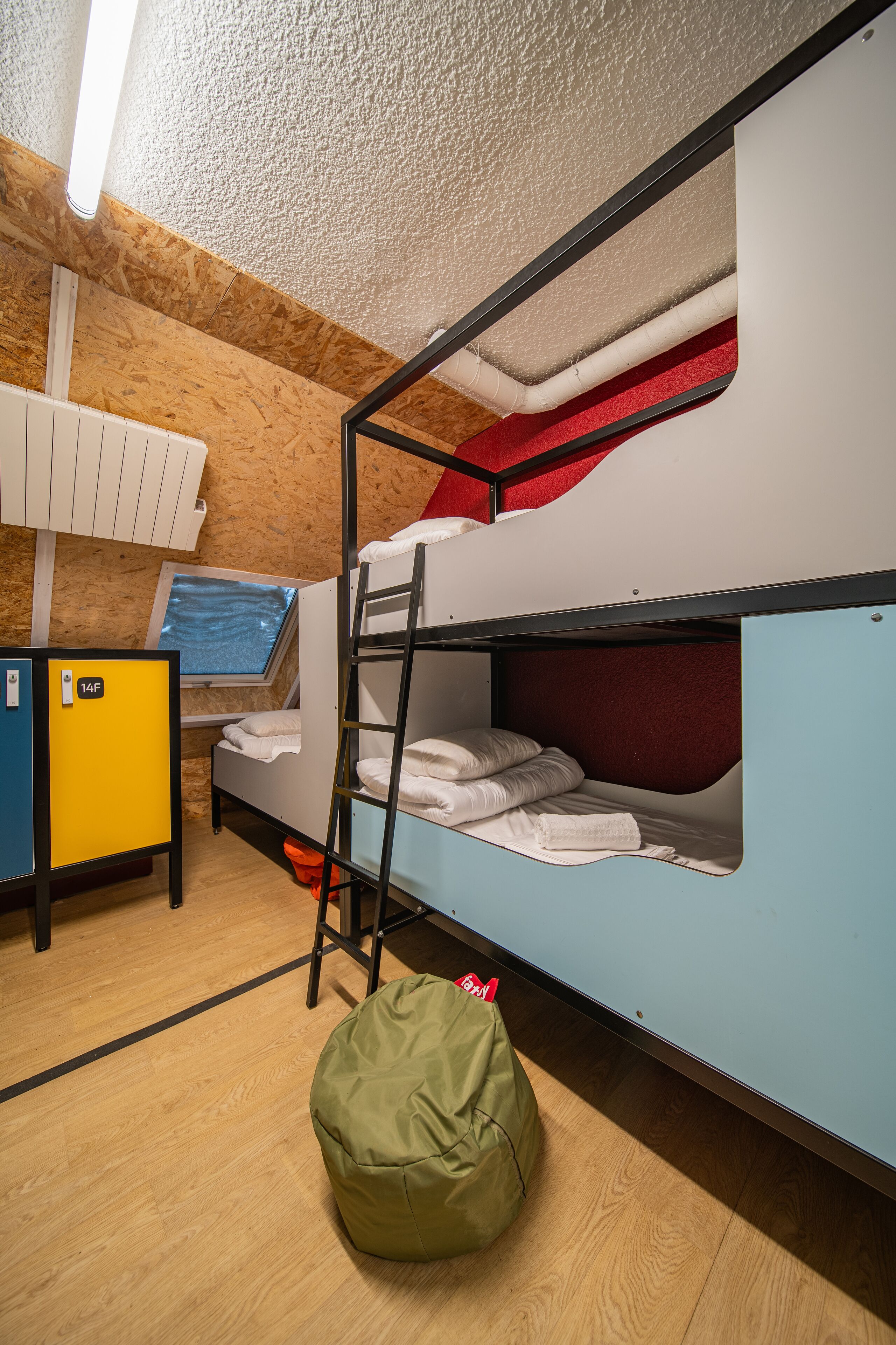 Habitación con literas, piso de madera, un escritorio con computadora y un sillón de pie verde.