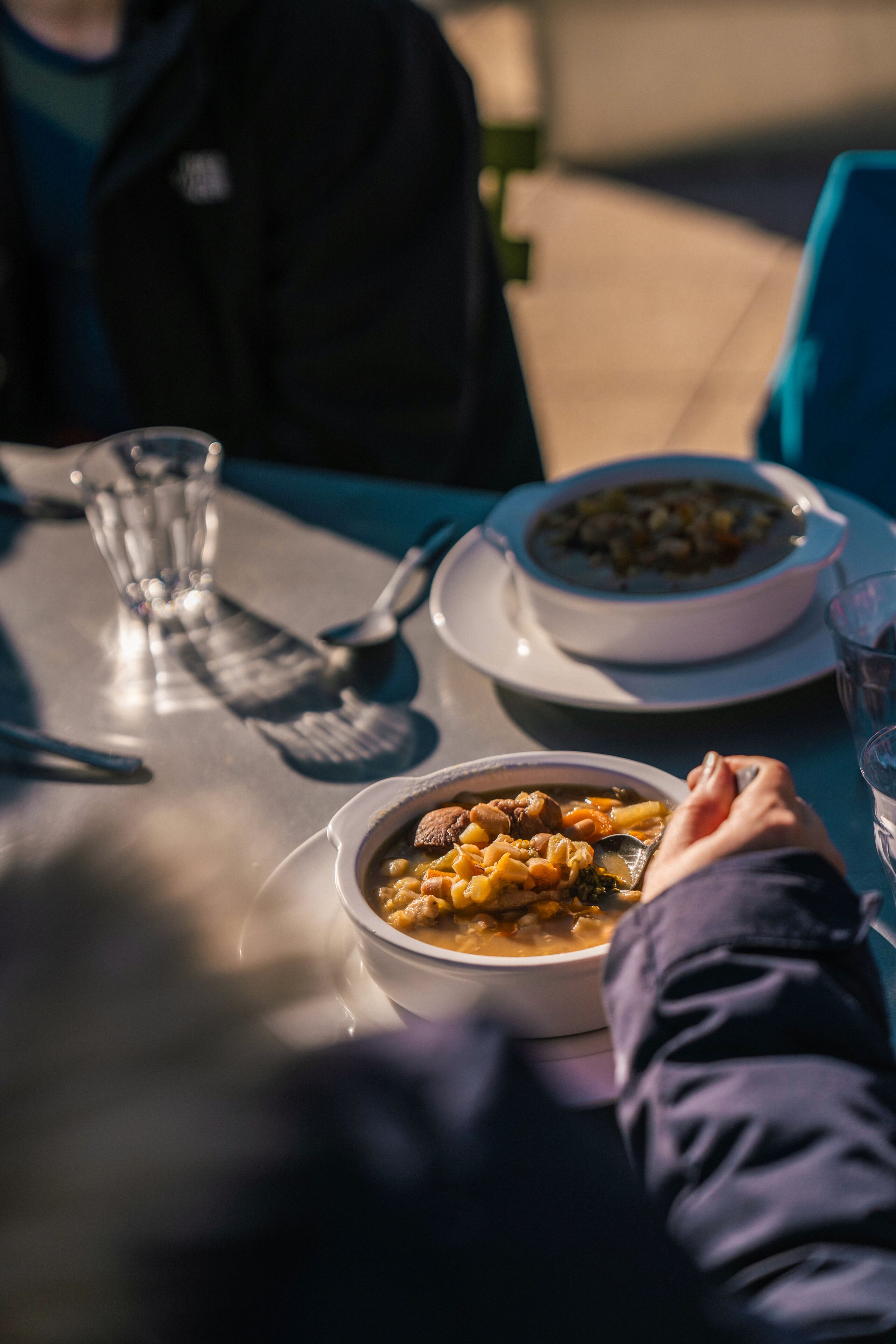 A dining table with two bowls of soup and a glass of water.