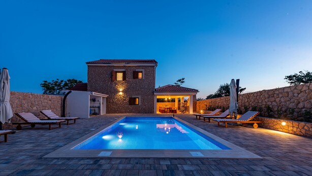 Una piscina con sillones de descanso, un edificio de piedra y un muro de piedra.