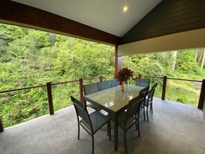 A covered outdoor dining area with a table and chairs, surrounded by a wooden railing, overlooking a lush green forest. - 6 bed, 4 bath, 3 level renovated Barn, 1400m to Bowral centre, 320m2, peaceful. (Bowral)
