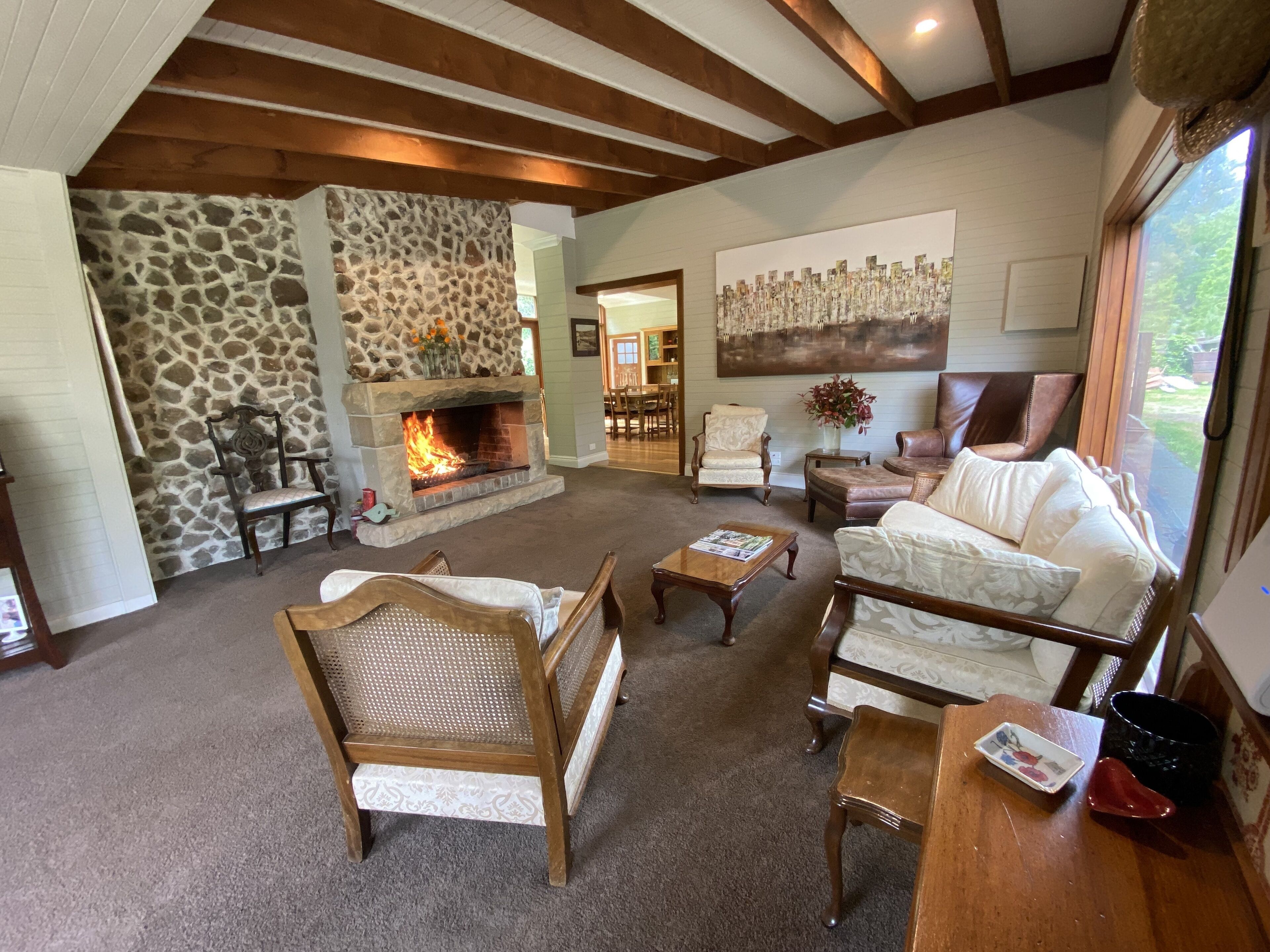 A cozy living room with a stone fireplace, wooden furniture, and a large painting on the wall.