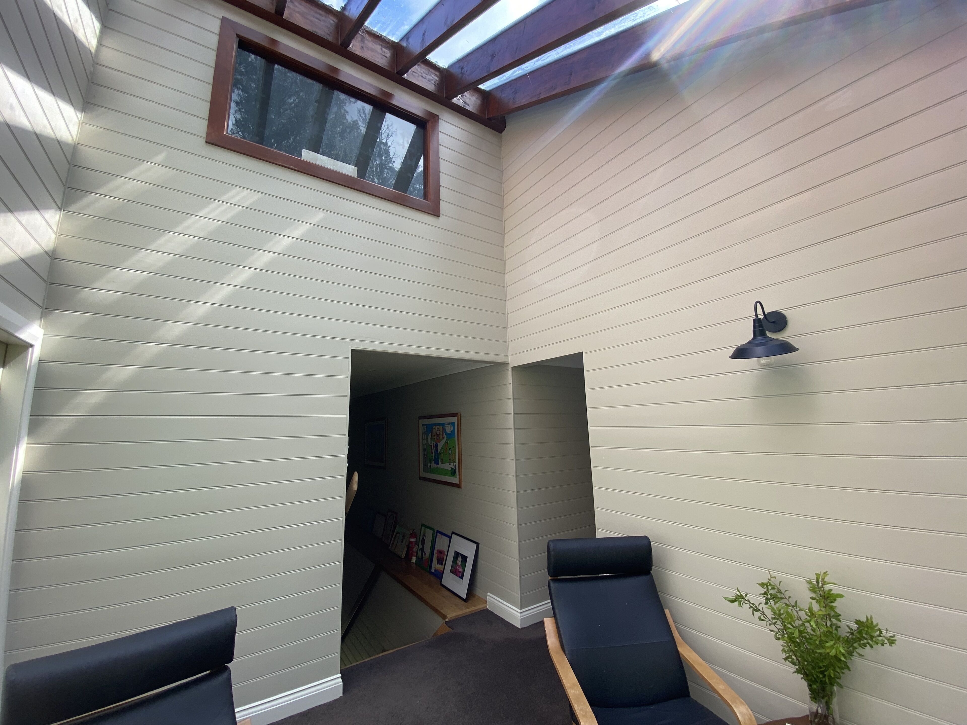 A room with a skylight, a dark blue chair, a small table, and a potted plant.