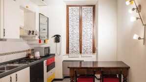 Une cuisine compacte équipée d’une cuisinière, d’un four à micro-ondes et de placards. On y trouve une table à manger avec deux chaises et une fenêtre agrémentée de rideaux décoratifs.
