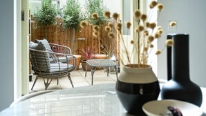 A modern living room with a glass table, a black vase, and a wicker chair.