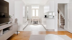 A modern kitchen with white cabinetry, a dining area with a table and chairs, and a staircase leading to another level.