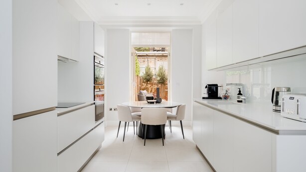 A modern kitchen with white cabinetry, a central island with chairs, and a view of the outdoor garden.