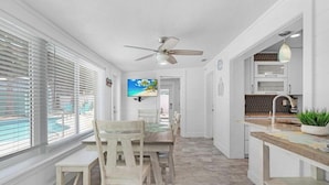 A modern kitchen with a dining area, a ceiling fan, and a view of the ocean through large windows. - Surf Drive Paradise – Oceanview Pool Home Just Steps from the Beach (St. Augustine Beach)