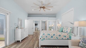 A bedroom with a bed, dresser, ceiling fan, and a view into another room. - Surf Drive Paradise – Oceanview Pool Home Just Steps from the Beach (St. Augustine Beach)