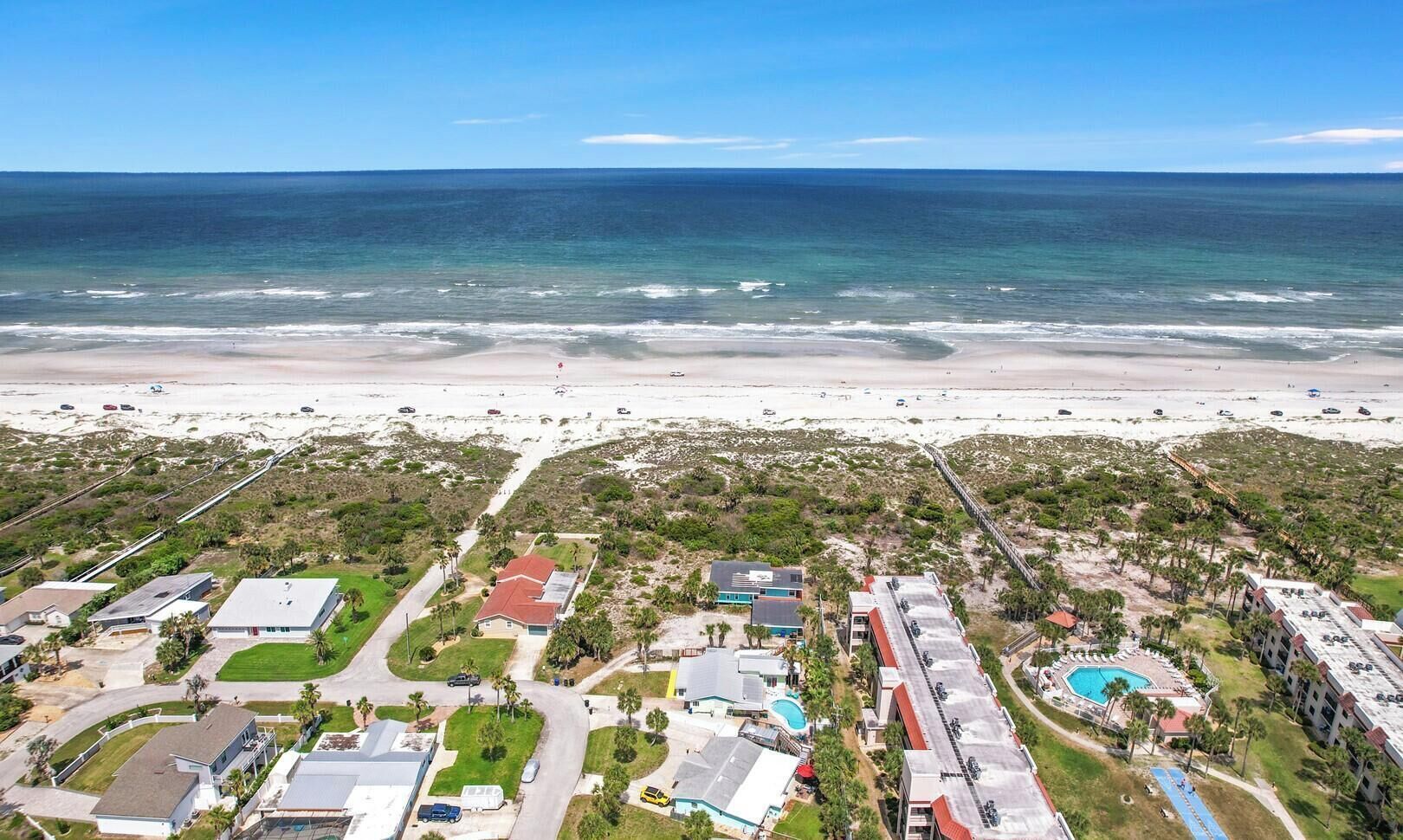 Vue aérienne d’un quartier résidentiel situé sur la côte, avec des maisons, une plage et une piscine.