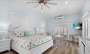 Une chambre avec un lit, un ventilateur de plafond, une télévision et une porte-fenêtre coulissante donnant sur l’extérieur.