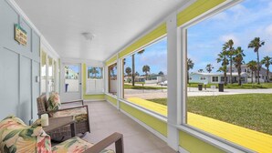 A covered outdoor area with a view of a residential neighborhood, a table with chairs, and a door. - Surf Drive Paradise – Oceanview Pool Home Just Steps from the Beach (St. Augustine Beach)