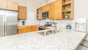 Una cocina moderna con encimeras de granito, electrodomésticos de acero inoxidable, armarios de madera y un ventilador de techo.
