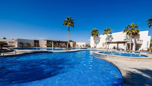 Una piscina con bordes de azulejos, palmeras y arquitectura moderna.