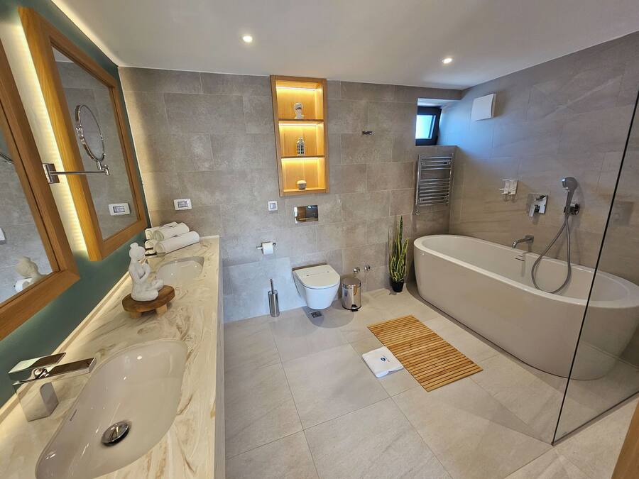 A modern bathroom with a bathtub, a sink, and a toilet. There are shelves with decorative items and a mirror.