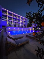 Un hotel moderno con piscina, sillones de descanso y un edificio de varios pisos con balcones.