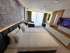 Habitación de hotel con dos camas, un escritorio, un televisor y un ventanal con cortinas.
