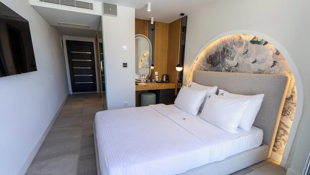 A modern hotel room with a large bed, a vanity with a mirror, and a unique wall design. - The New Hotel Mediteran Villa Edition (Ulcinj)