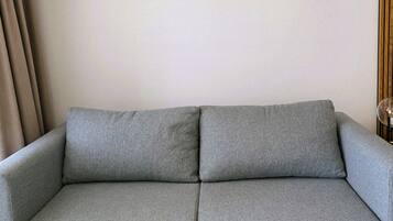 A grey sofa with a wooden frame, two wall-mounted picture frames, and a curtain on the left.