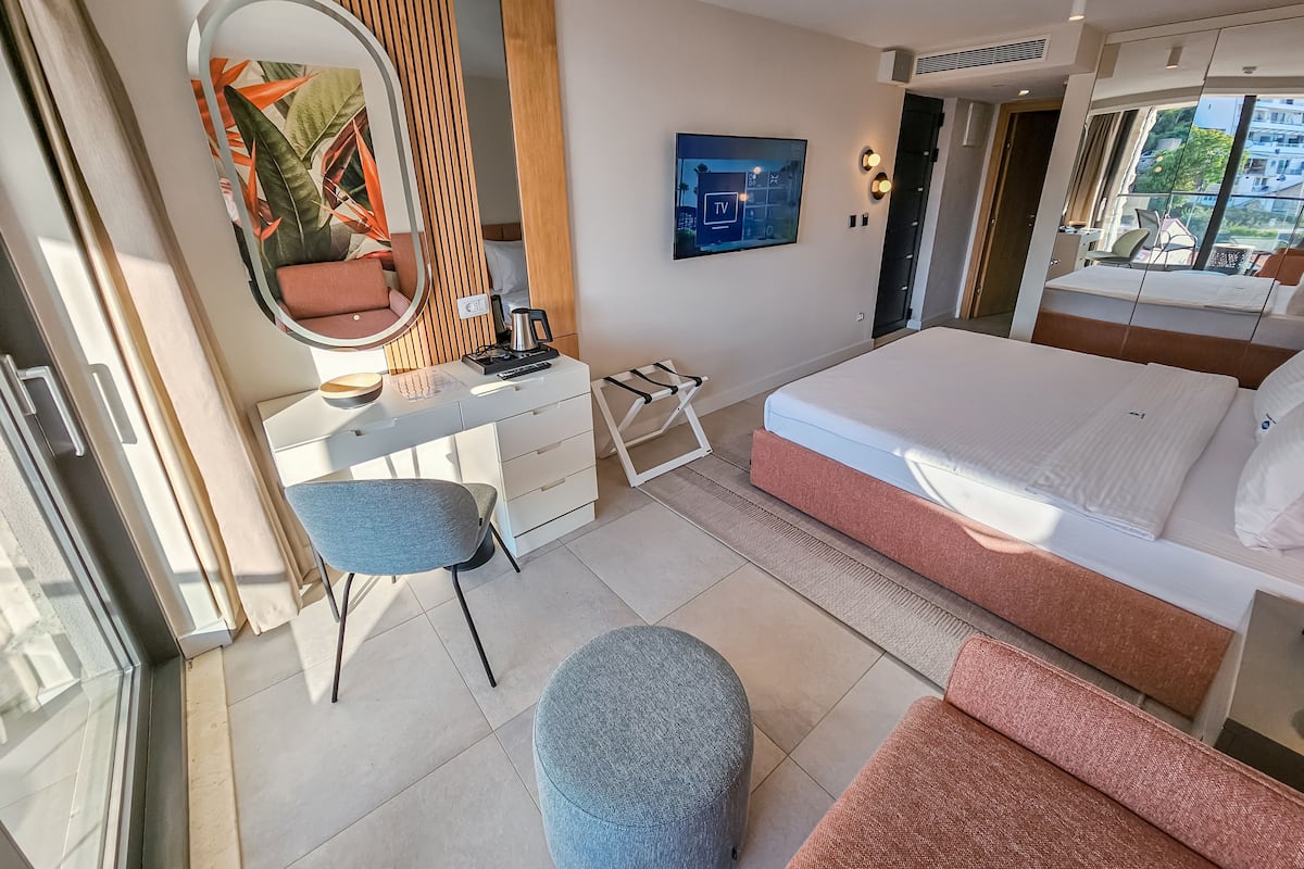 Ein modernes Hotelzimmer mit Bett, Schreibtisch mit Stuhl, Spiegel und Fernseher.