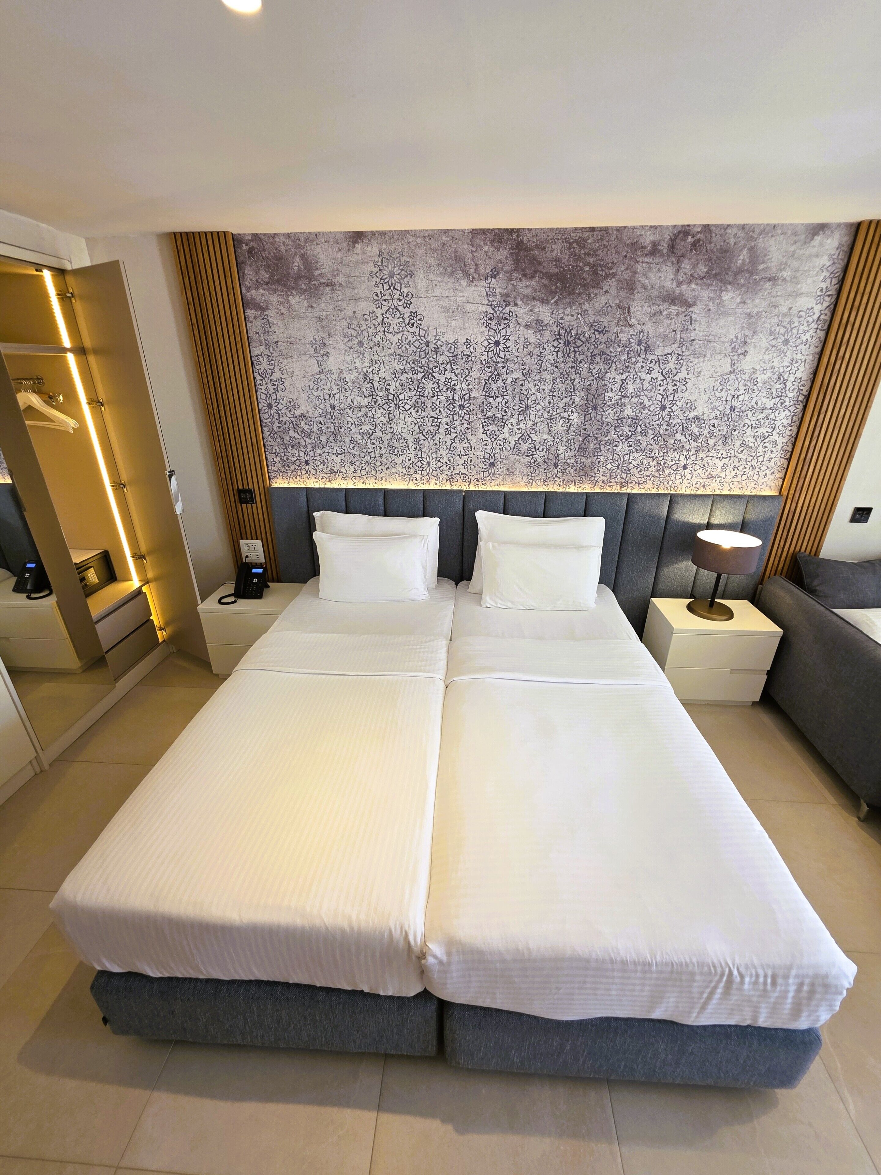 A double bed with a grey headboard, bedside tables with lamps, and a patterned wall behind.