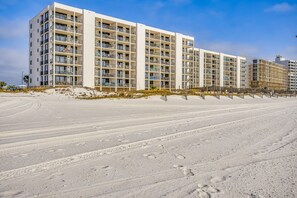 A beachfront hotel with multiple floors, balconies, and a sandy beach in the foreground.