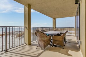 Un balcon abrité, doté d’une table et de chaises en osier, qui donne sur une plage protégée par une rambarde en métal.