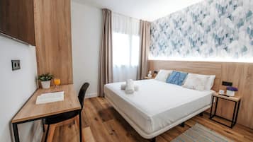 A modern hotel room with a wooden bed, a desk, and a small table with a plant and a glass of orange juice.